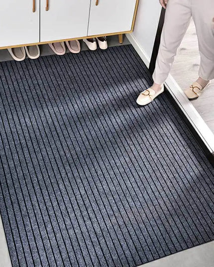 Person entering a room with a black doormat on a gray floor.