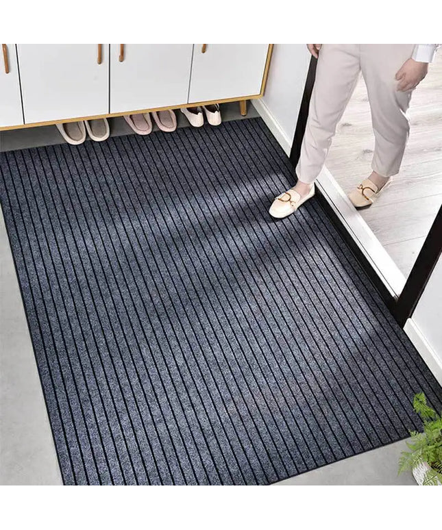 Person entering a room with a black doormat on a gray floor.