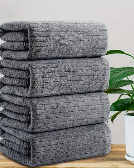 Stack of gray towels on a wooden surface with a plant in the background