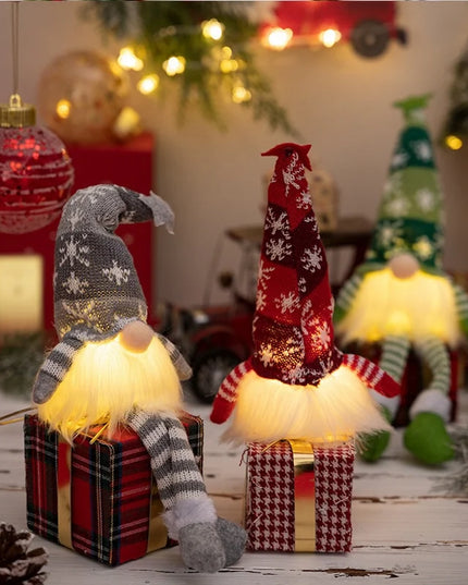 Decorative gnomes with lights on small gift boxes in a festive setting with Christmas trees and ornaments.