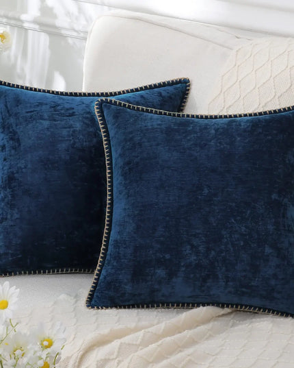 Two blue velvet pillows on a white couch with flowers in the background