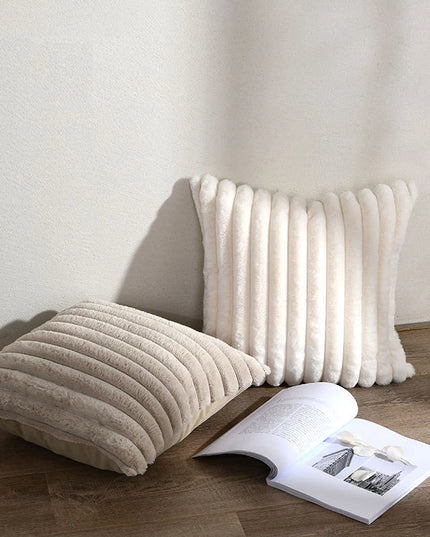 Two textured pillows on a wooden floor with an open book beside them.