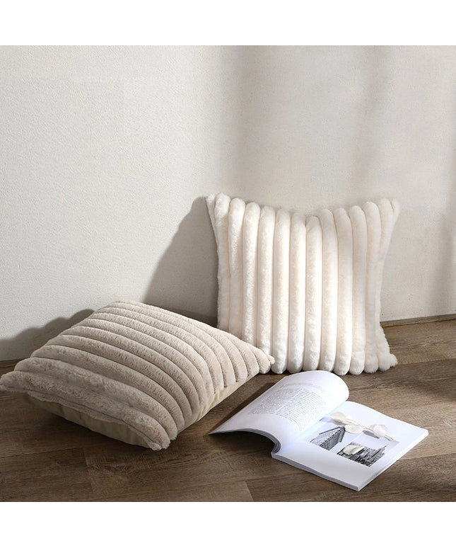 Two textured pillows on a wooden floor with an open book beside them.