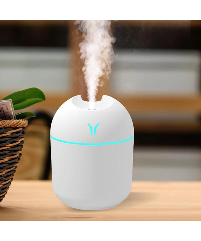 White humidifier with blue light on a wooden surface, emitting mist.