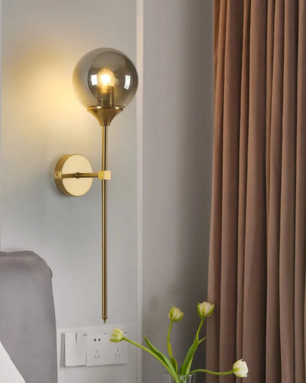 Gold wall sconce with glass shade on a gray wall next to brown curtains.