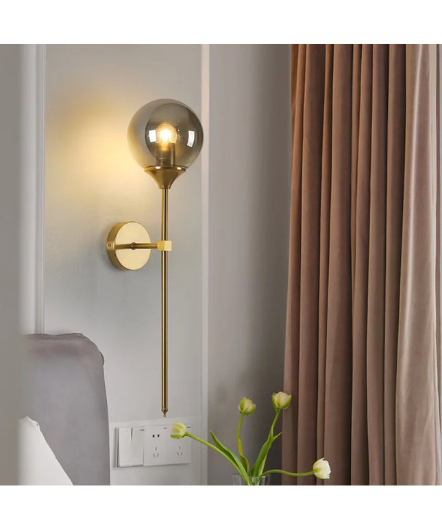 Gold wall sconce with glass shade on a gray wall next to brown curtains.